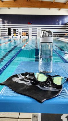 a water bottle and goggles sitting on top of a blue table next to a swimming pool