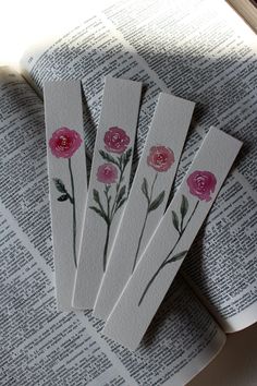 four bookmarks with pink flowers on them sitting on top of an open book,