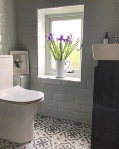 a white toilet sitting next to a bathroom sink under a window with purple flowers in it