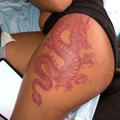 a woman laying in bed with a dragon tattoo on her arm and leg, holding a cell phone