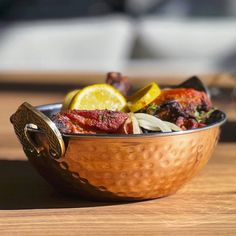 a copper bowl filled with lots of different types of food on top of a wooden table