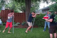 three men in the yard with one holding a cake on a stick and another carrying a box