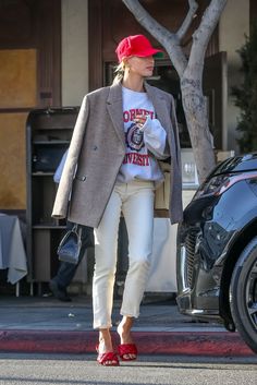 a woman walking down the street wearing white pants and a red hat with her hand in her pocket