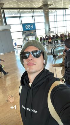 a man wearing sunglasses and a hat in an airport with his hand up to the camera