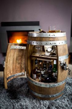 a wooden barrel with wine glasses and bottles in it sitting on a rug next to a fireplace