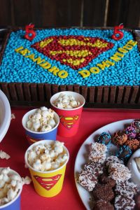 a superman themed birthday party with popcorn, cake and desserts on a red table