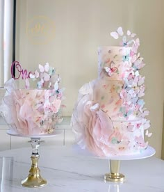 two wedding cakes decorated with pink and blue flowers on top of a white marble counter