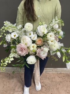 a woman holding a bouquet of white and pink flowers in her hands while standing next to a wall