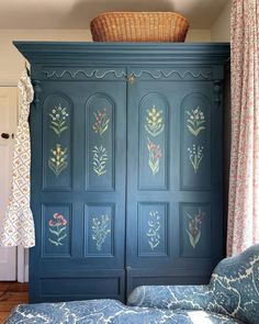 an armoire painted in blue with flowers and leaves on the doors is next to a bed