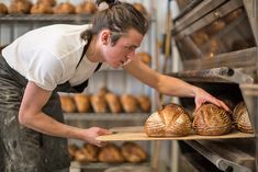 a woman reaching into an oven with some breads in front of her and looking at it