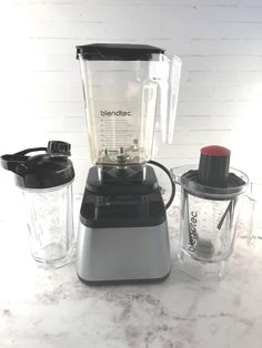 three blenders sitting next to each other on top of a marble countertop in front of a white brick wall