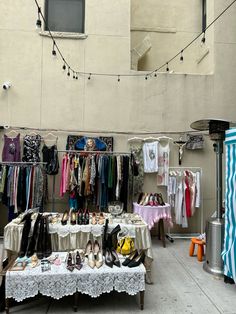 an outdoor market with clothes and shoes for sale on the tables in front of it