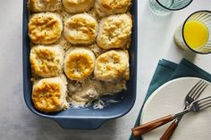 a blue casserole dish filled with biscuits and cheese next to glasses of orange juice