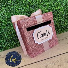 a pink card box with a bow on it sitting on top of a wooden table