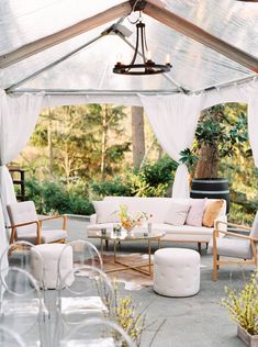 an outdoor living area with white furniture and drapes on the ceiling, surrounded by greenery