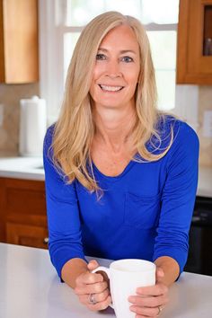 a woman sitting at a kitchen table holding a coffee cup