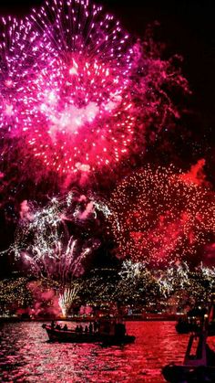 fireworks are lit up in the night sky over water with boats floating on the water