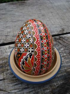 an egg painted with colorful designs in a bowl on a wooden table outdoors, ready to be eaten