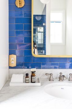 a bathroom with blue tile and gold accents on the mirror above the sink is a soap dispenser