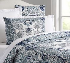 a bed with blue and white comforters in front of a window, next to pillows