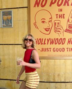 a woman walking down the street with a drink in her hand and a sign behind her