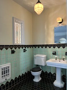 a bathroom with green and black tiles on the walls, toilet and sink in it