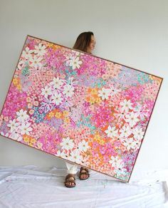 a woman holding up a large painting with flowers on it