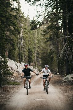 two people riding bikes down a dirt road