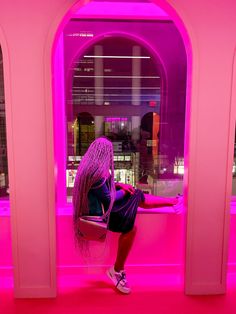 a woman sitting on a window sill in front of a pink wall at night