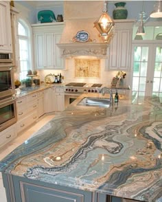 a large kitchen with marble counter tops and white cabinetry, along with stainless steel appliances