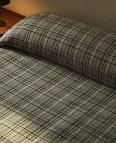 a bed with a plaid comforter on top of it next to a night stand