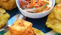 a plate with some food on it next to a bowl of vegetables and bread rolls