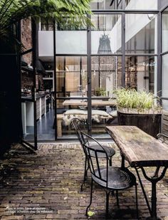 an outdoor dining area with wooden tables and chairs, surrounded by large glass windows that look out onto the courtyard