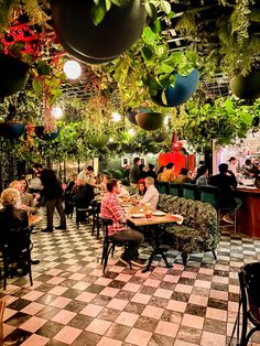 people sitting at tables in a restaurant with plants hanging from the ceiling