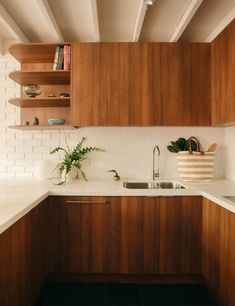 a kitchen with wooden cabinets and white counter tops, plants in a basket on the sink