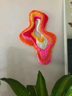 a crocheted object hanging on the wall next to a potted plant