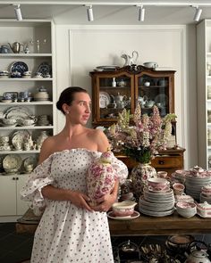 a woman standing in front of a table filled with plates and vases on it