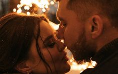 a man and woman kissing in front of christmas lights