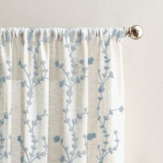 a curtain with blue flowers on it hanging from a metal rod, in front of a white wall