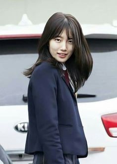 a woman in a suit and tie standing next to a white car with her hand on her hip