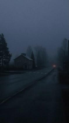 an empty street in the middle of a foggy night with houses on either side