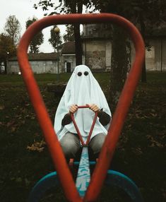 a person dressed as a ghost riding on top of a blue wheelbarrow in the grass