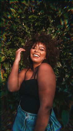 a woman standing in front of a bush with her hands on her head and smiling