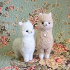 two stuffed llamas sitting next to each other on a floral cloth covered surface