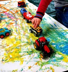 a child is playing with toy trucks on a table covered in paint and crayons