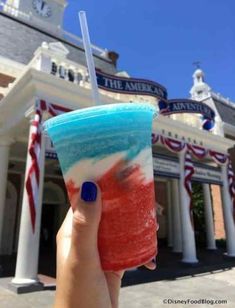 a hand holding up a drink in front of the american adventure building at disney world