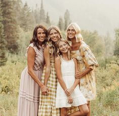 four women are posing for a photo in front of some trees and grass with their arms around each other