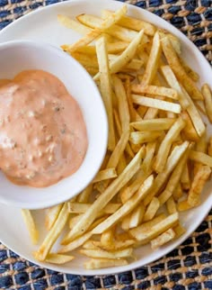 a white plate topped with french fries next to a bowl of dipping sauce on top of it