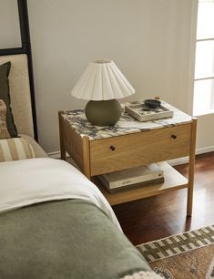 a nightstand with a lamp on top of it next to a bed in a bedroom