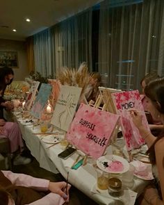 a group of people sitting around a table with paintings on it and candles in front of them